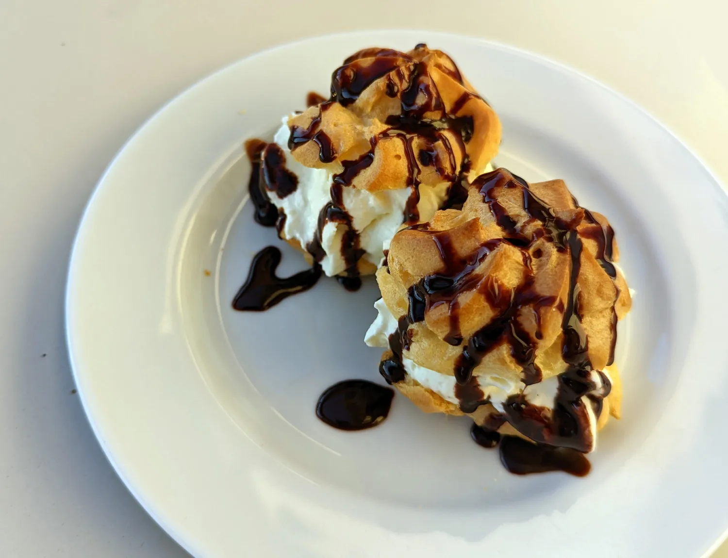 Gefüllte Brandteigkrapferl mit Schlagobers und Schokosauce auf einem Teller.