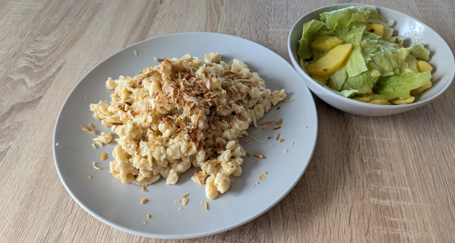 Teller mit Käsespätzle, gerösteten Zwiebeln und Salat.