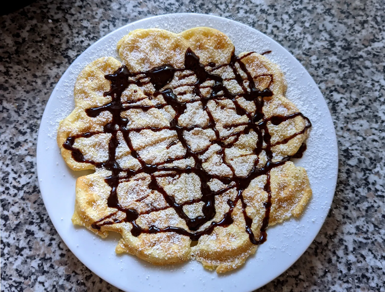 Goldene Waffeln mit Staubzucker und Schokosauce.